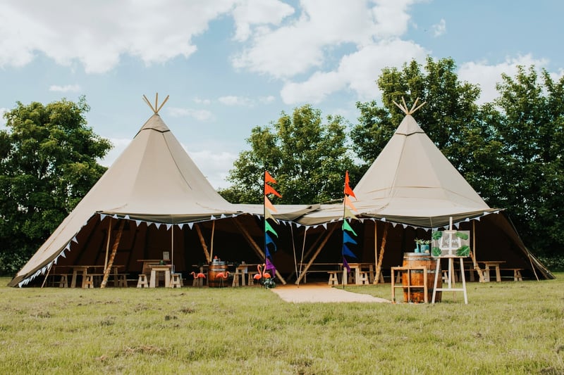 exterior of a tipi wedding tent set up for a wedding, including colourful festival flags.
