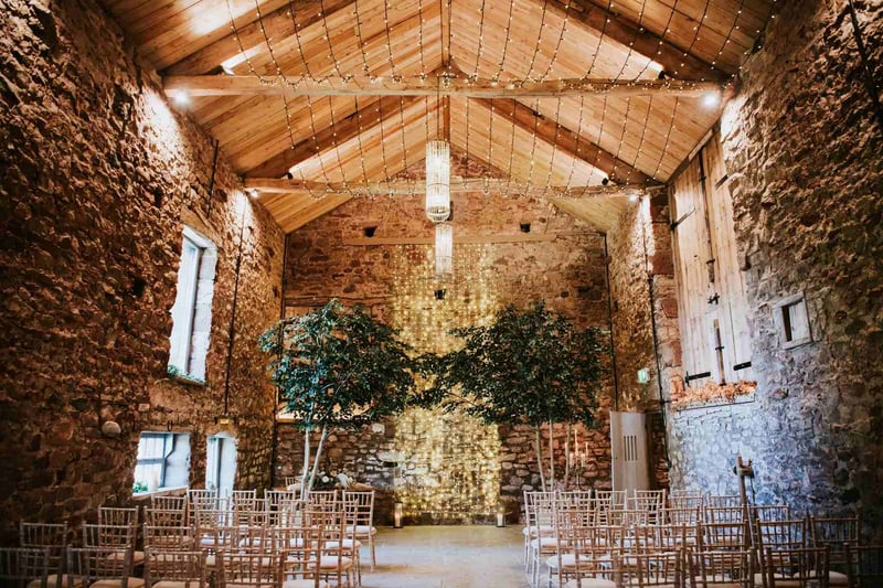 Rustic wedding ceremony set up in a brick barn with a wall covered in cascading fairy lights