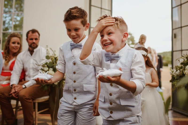 Two page boys walking down the aisle at a wedding as one comically places his hand on his forehead in a panic