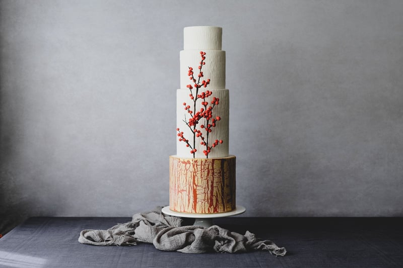 a four-tiered modern sculptural wedding cake with simple red berry decoration and textured icing.
