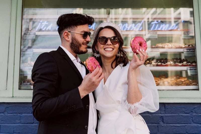 A bride and groom posing with pink iced doughnuts