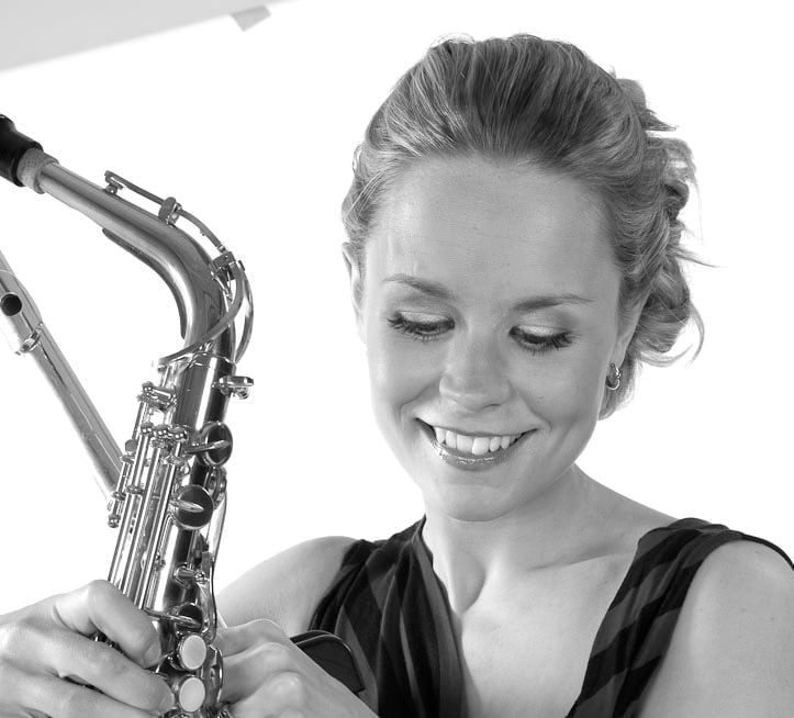 a female saxophonist smiling and looking down as she holds her saxophone.