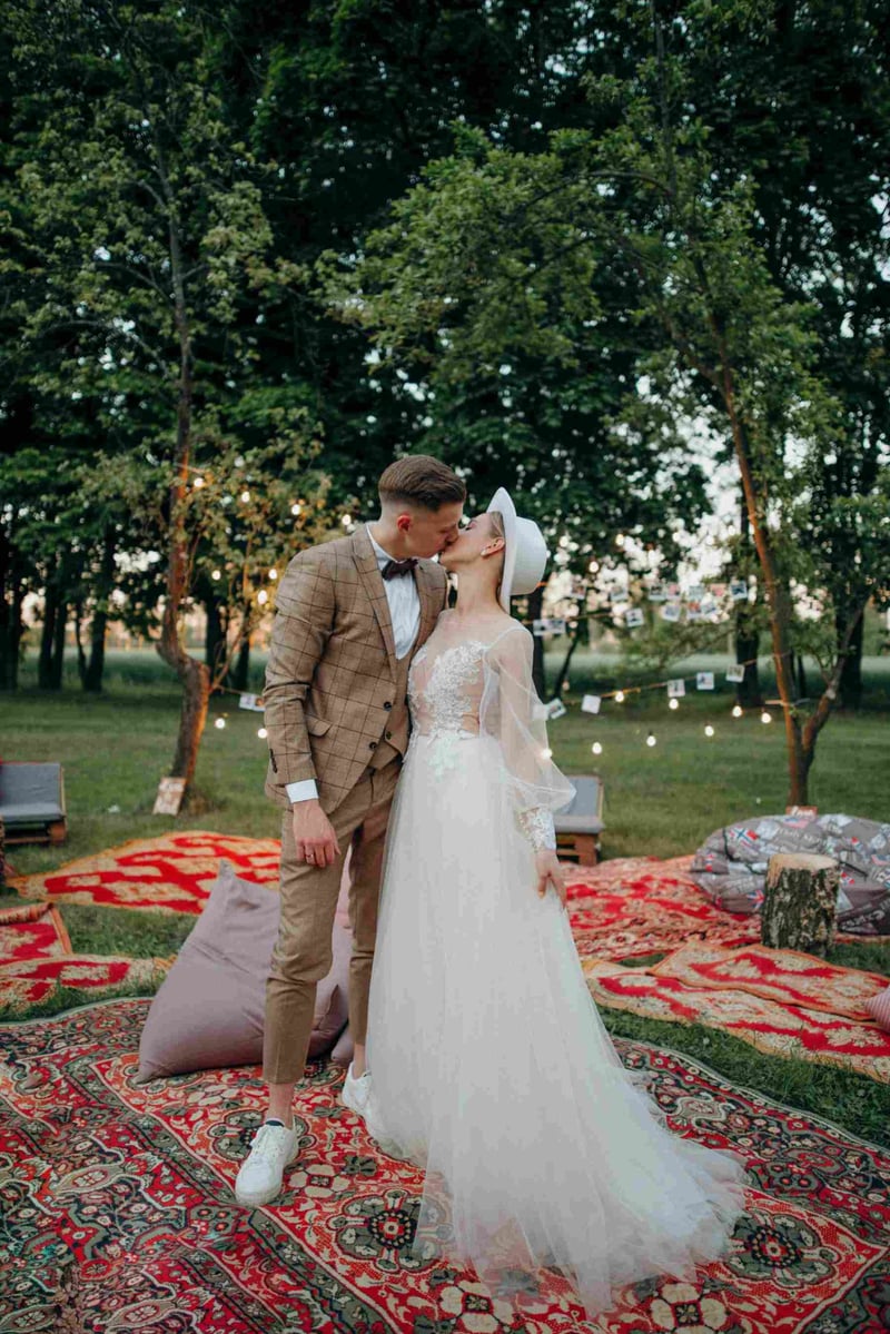 A bride and groom share a romantic kiss at their boho outdoor wedding during sunset, standing on colourful patterned rugs