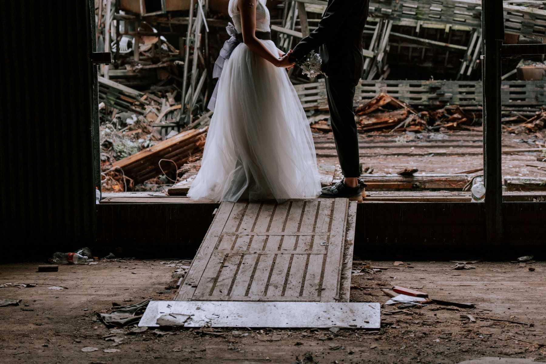 Shoulders-down photo of a bride and groom holding hands in a rustic barn wedding setting