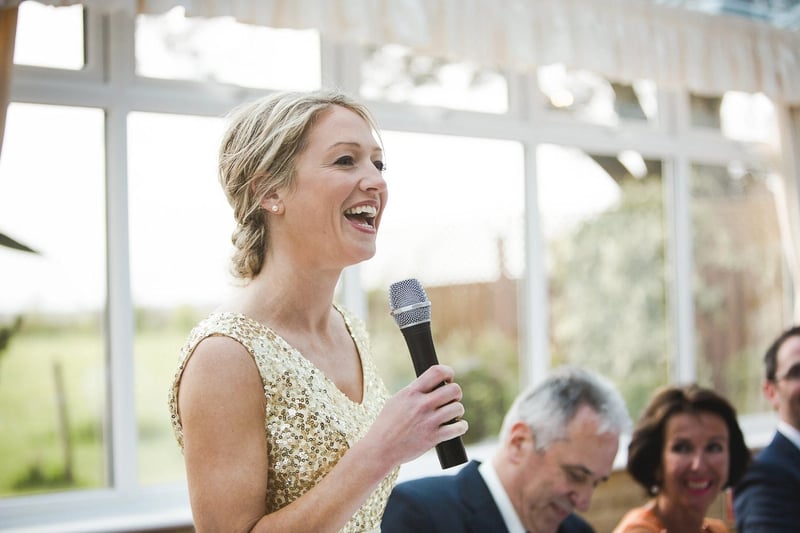 A maid of honour in a gold sequinned dress giving a speech at a wedding