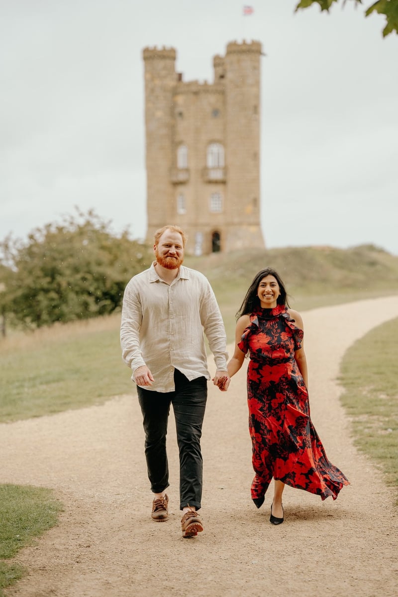 an engaged couple walk hand in hand as they smile at the camera.