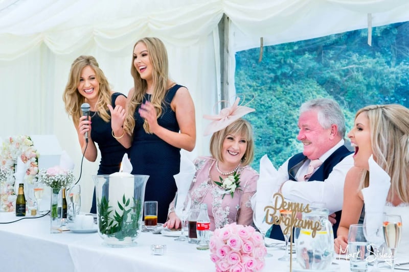 A bridesmaid and maid of honour giving a speech as the bride and her parents laugh