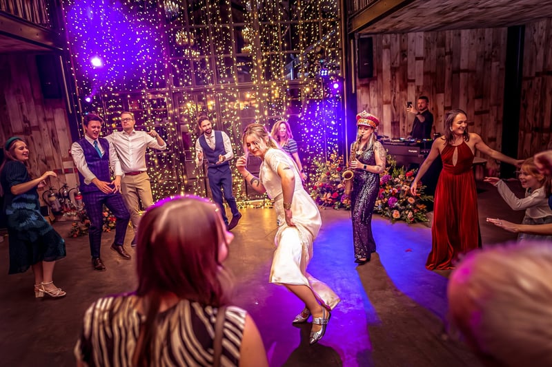 a bride dances in the centre of the dancefloor as guests surround her and a saxophonist performs at the side.