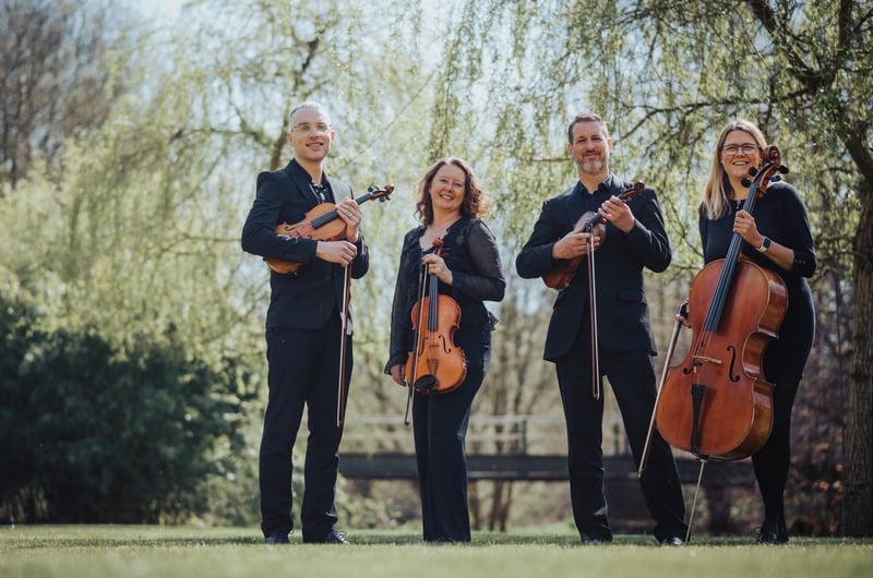 a group of four string musicians smile into the camera as they hold their string instruments.