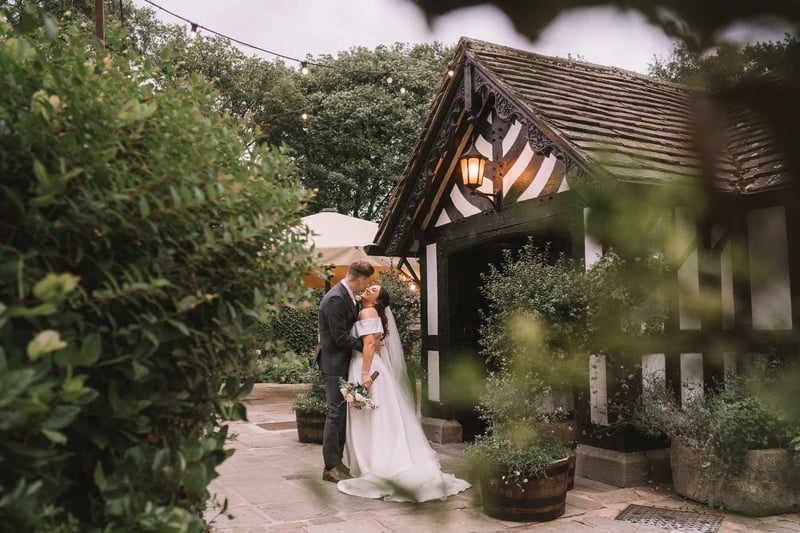 Couple sharing a romantic moment outside a black-and-white timber-framed Tudor wedding venue with festoon lights at dusk