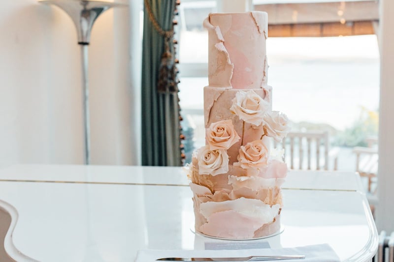 a pale pink three tier wedding cake with paper-like textural details and pale pink roses.