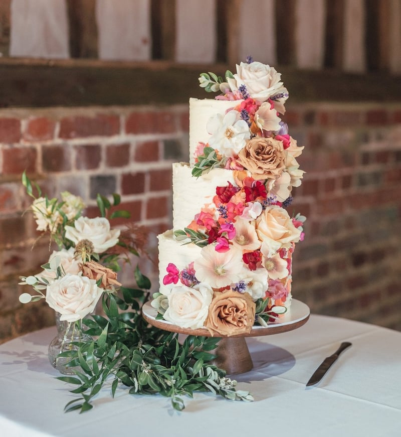 a three tier wedding cake with a cascade of colourful flowers.