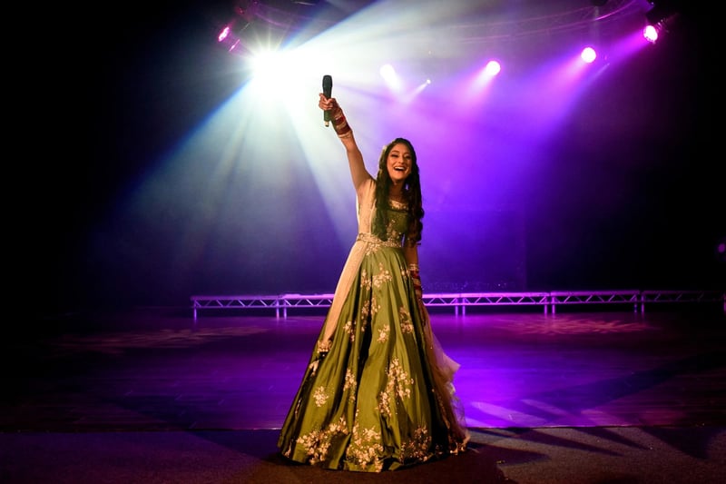 A maid of honour in traditional indian wedding attire holding up a microphone on a stage