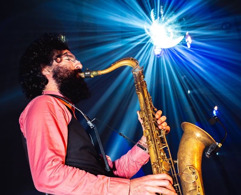 a bearded saxophonist performs with lights in the background.