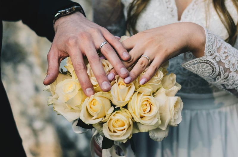 Bride and groom resting their hands on a bouquet of white roses, showing off their wedding rings