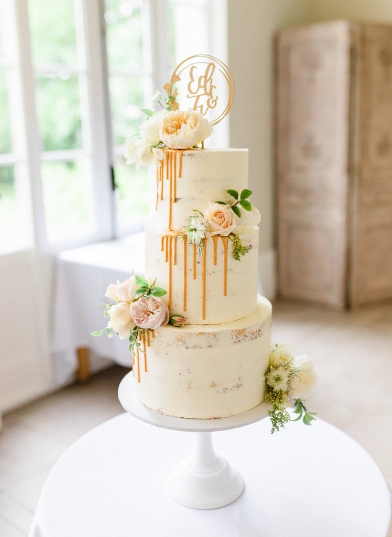a three-tier buttercream wedding cake with gold drip icing detail and cream-coloured flowers.