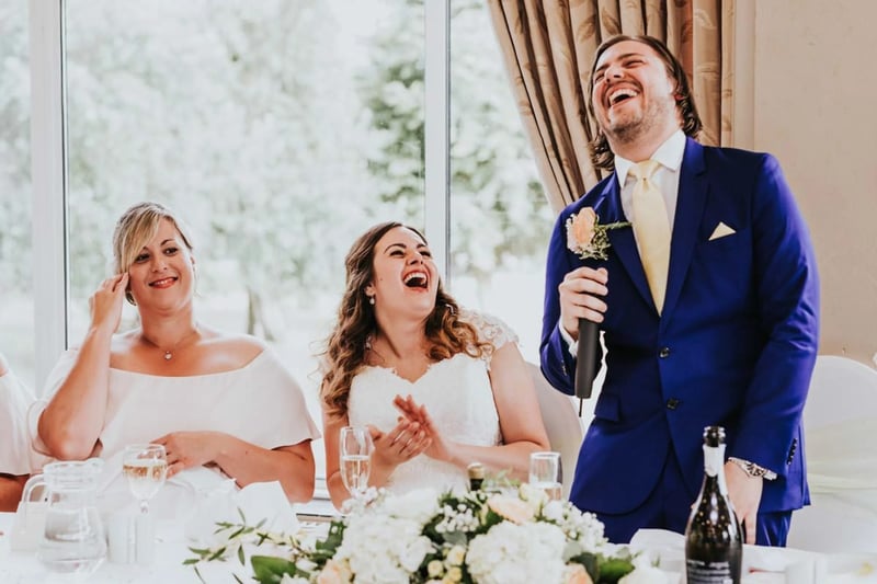 Best man laughing as he gives a speech to two brides who are also laughing