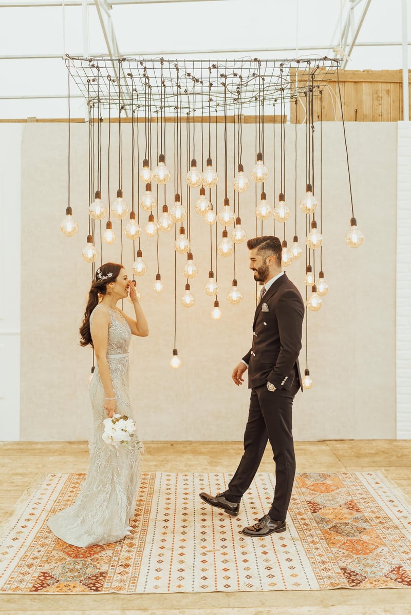 Bride and groom smiling at each other under industrial style edison light bulbs hanging down