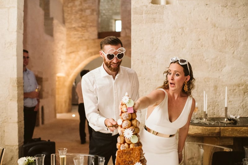 A couple laughing as they cut into a croquembouche wedding cake