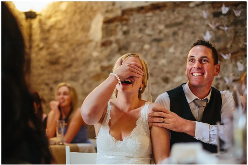 Bride covering her eyes and laughing at a best man's speech