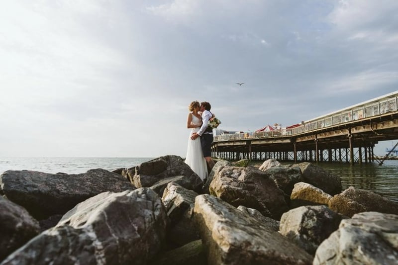 Bride and groom kissing on a beach next to a pier in kent