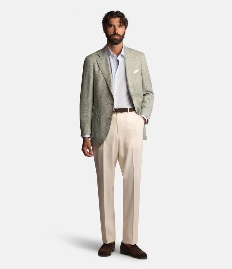 a male model wearing a green glencheck blazer with cream tailored trousers and a light blue shirt.