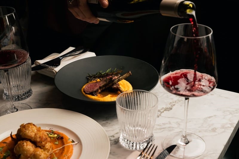 red wine being poured into a glass next to plates of food in a restaurant.