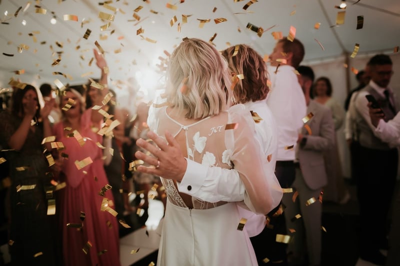 a newlywed couple on the dancefloor with wedding guests as confetti falls.
