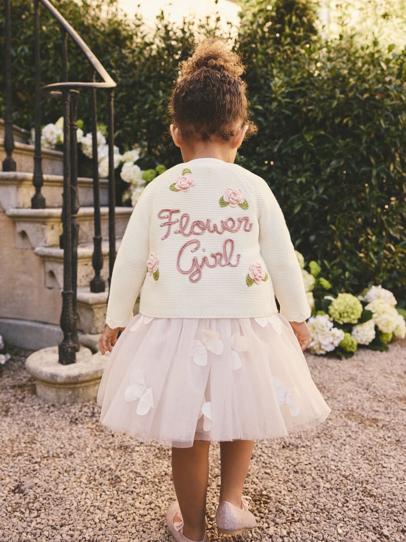 a young flower girl wearing a knitted cardigan that reads 'flower girl' on the back.