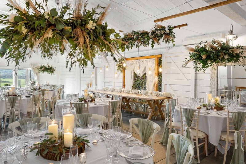 Rustic barn wedding reception with sage green chair sashes and hanging pampas grass florals