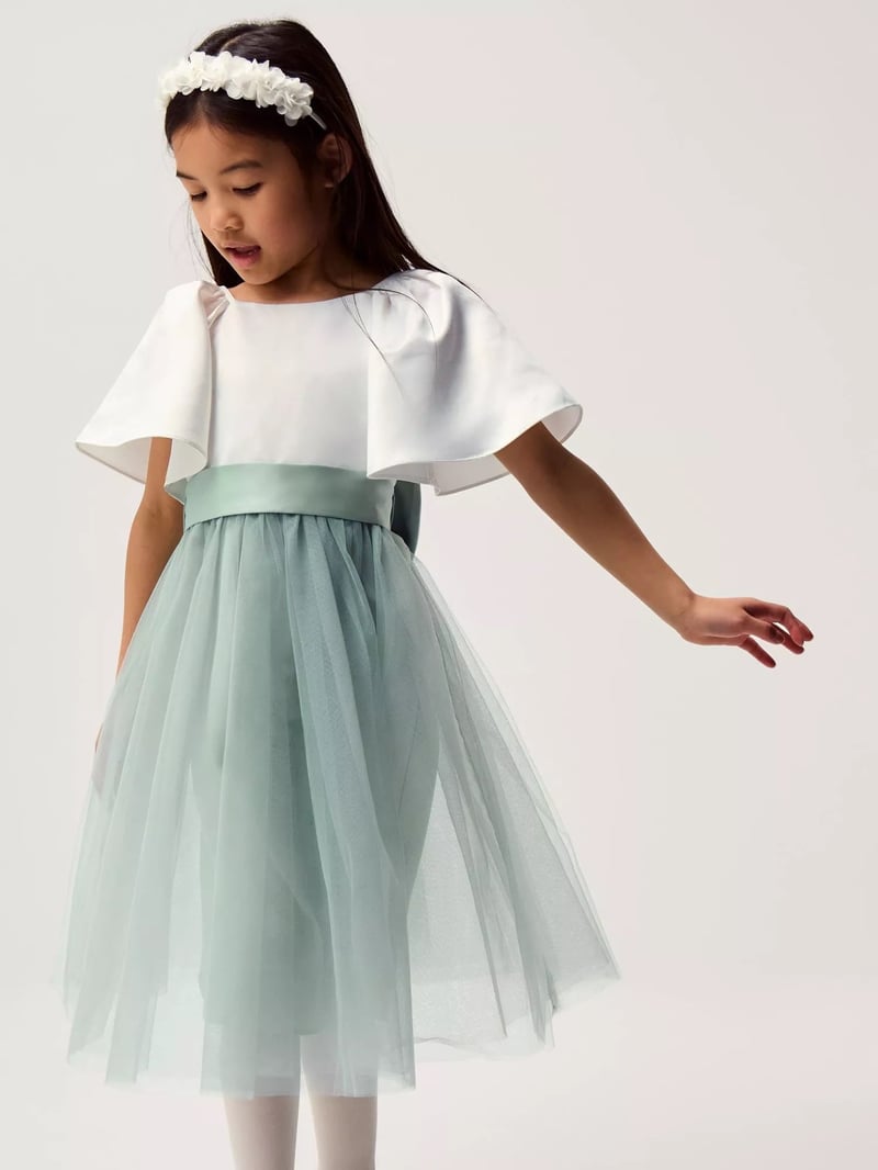 a child model wears a sage green and white flower girl dress with tulle skirt.