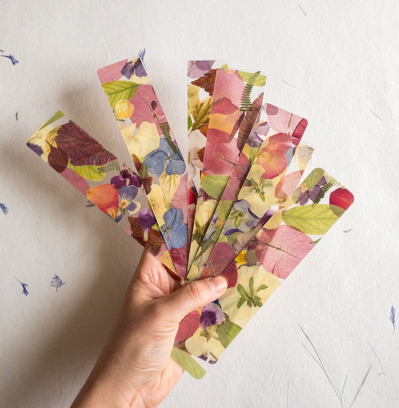 a hand holding a selection of pressed flower bookmarks.