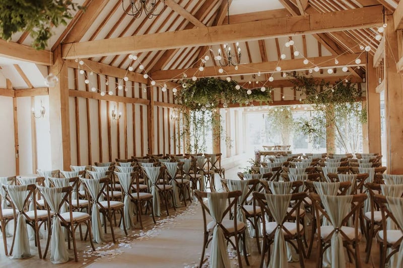 Oak-framed barn wedding ceremony space with festoon lights and hanging greenery