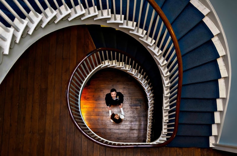 a newlywed bride and groom look up from the bottom of a winding staircase.