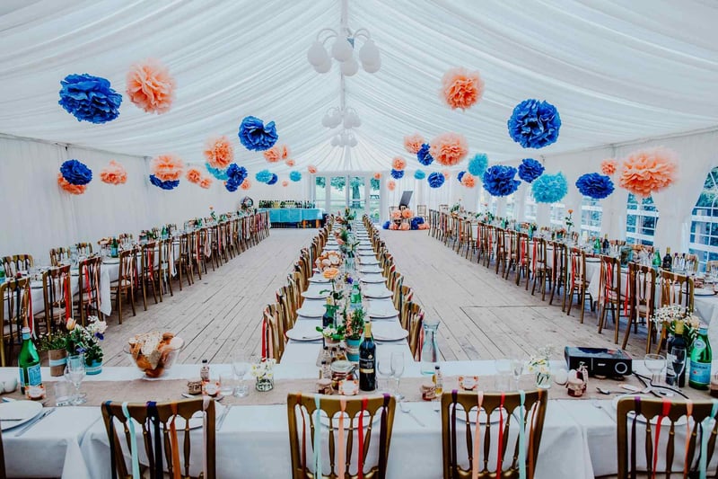 Interior of a wedding marquee with a draped fabric ceiling and peach and blue pom poms