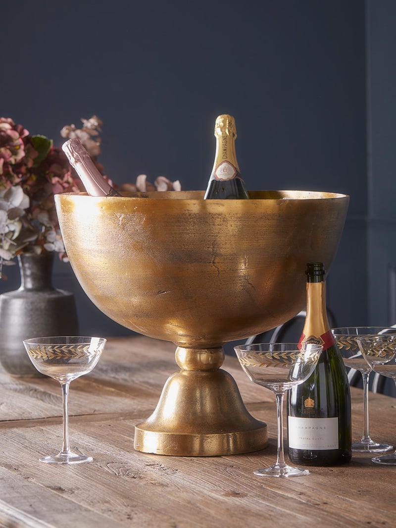 a footed antique brass wine cooler on a table with bottles of wine.