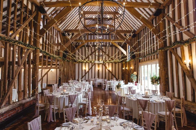 Oak-beamed barn wedding reception with dusky pink chair sashes and chandeliers