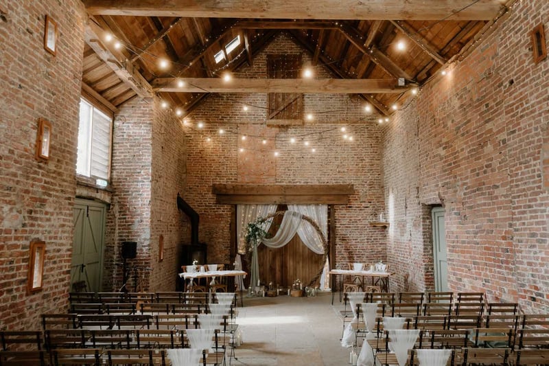 Exposed-brick barn wedding ceremony aisle with fairy lights and a round floral arch