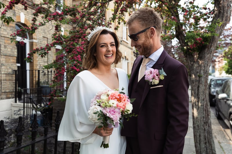 a newlywed bride and groom smile. the bride is holding a colourful bouquet.