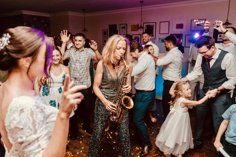 a female saxophone player performing on the dancefloor as wedding guests dance around her.