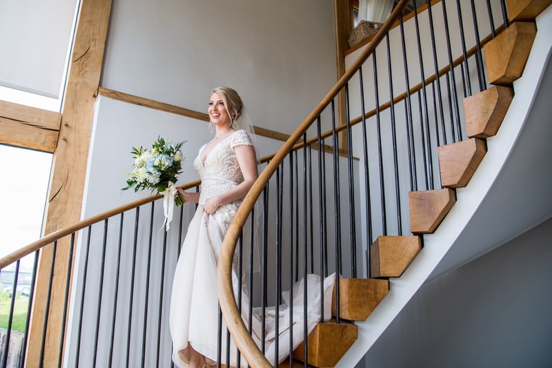a bride walking down the stairs of her wedding venue holding a bouquet.