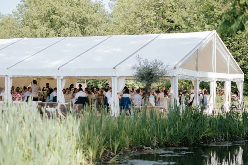 Wedding guests sitting inside a clear sided marquee by the water at Ardington House