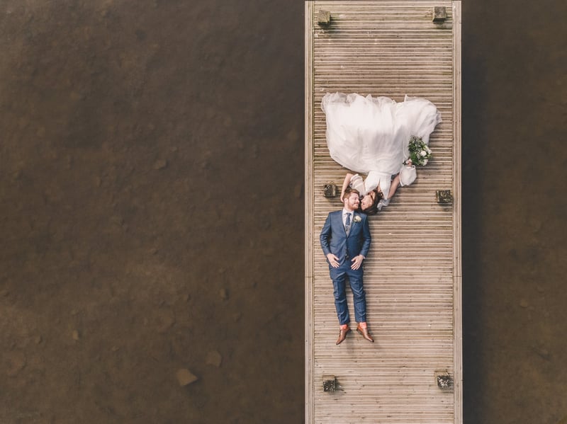 a bride and groom laying on a dock being photographed from above.