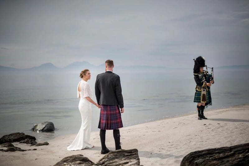 Bride and groom at a scottish beach wedding as a bagpiper plays