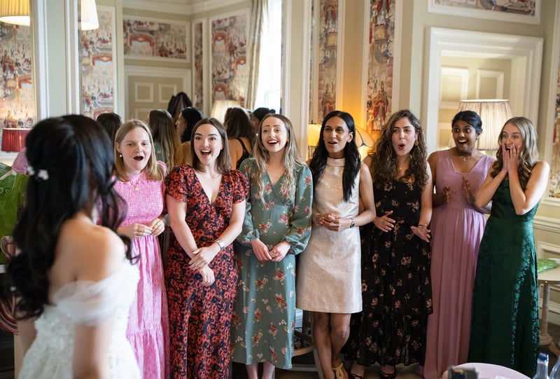 a group of friends smile and gasp as the bride reveals her dress. 