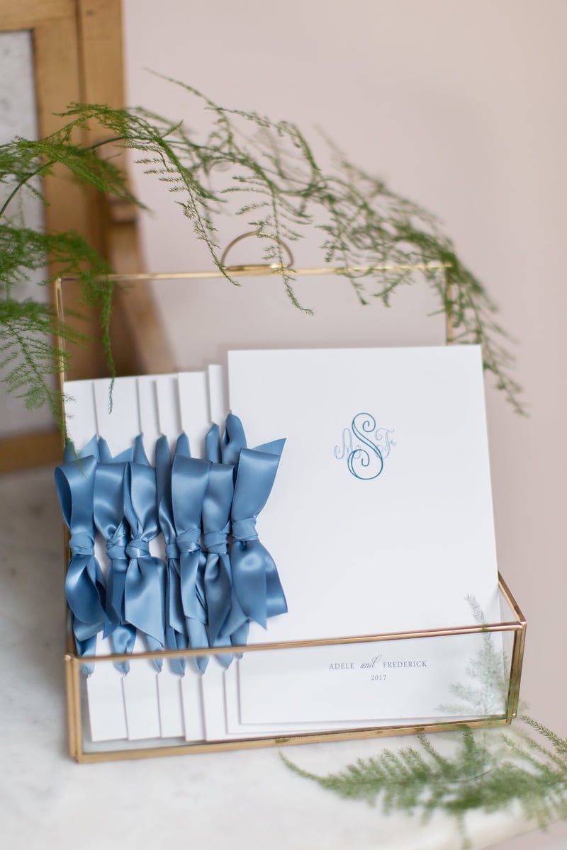 a stack of wedding order of service booklets tied with blue satin ribbon in a box.