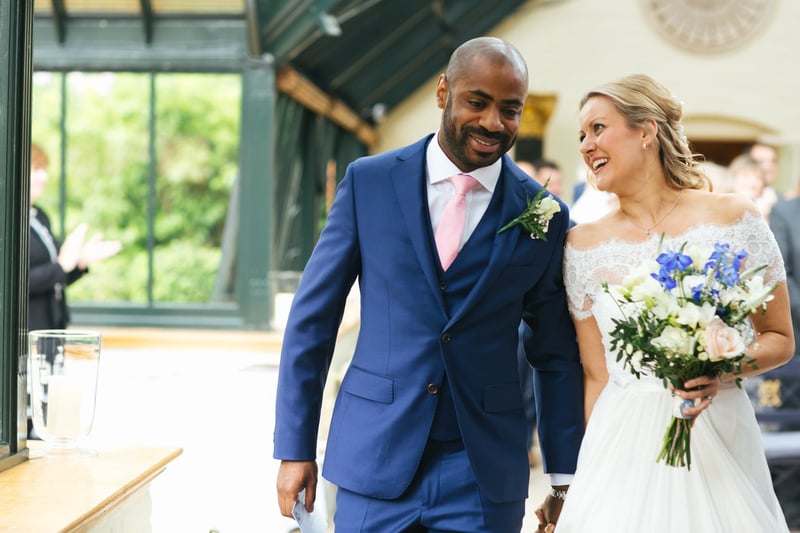 a groom in a navy wedding suit with pink tie walking with his bride.