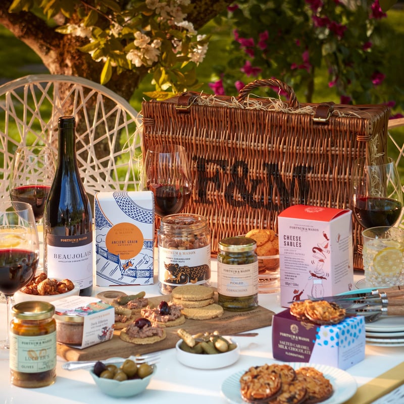 a fortnum and mason hamper basket with treats laid out like a picnic.