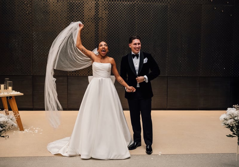 a newlywed bride and groom smile as they prepare to walk back down the aisle. The bride is holding her veil in the air and laughing.