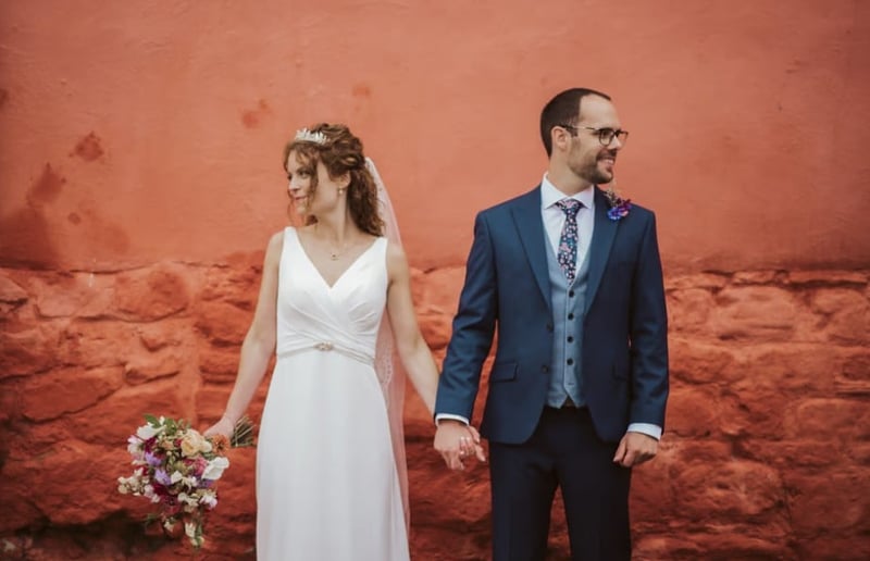 bride and groom posing hand in hand in front of a terracotta coloured wall